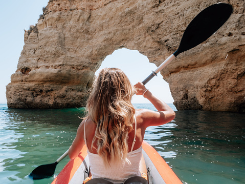 Rear view of woman paddling on red inflatable canoe in peaceful cove in Portugal