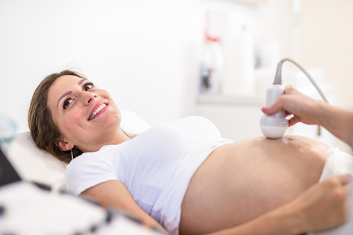 Unrecognizable doctor doing an Ultrasound exam of happy pregnant woman at Medical Clinic.