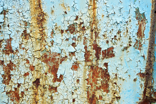 Peeling pale blue paint on a rusty metal surface. Interesting grunge texture. Obsolete door in decay.