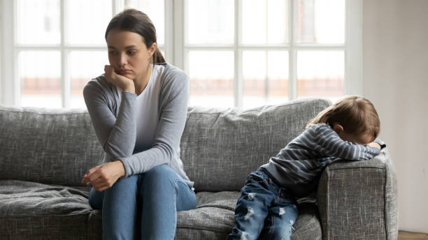 istock Stressed young mommy sitting separate on couch with offended son. 1267591975