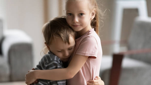 Little kid girl cuddling smaller brother at home. Head shot portrait of little kid girl cuddling smaller brother at home, showing love and care. Compassionate sister comforting soothing upset stressed boy in living room, siblings relations concept. empathy stock pictures, royalty-free photos & images