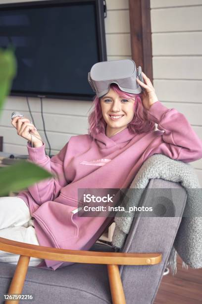Happy Hipster Teen Girl Wear Vr Headset Hold Controller Look At Camera In Chair Stock Photo - Download Image Now