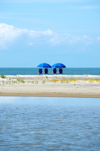 View of two blue beach chairs with umbrellas in front of the ocean.