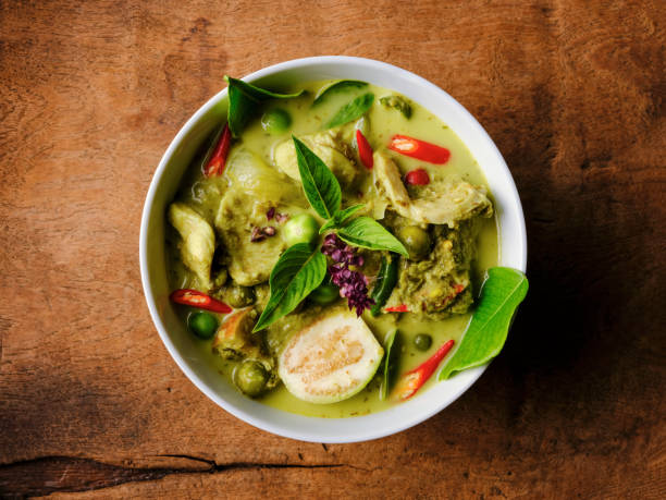 famous internationally renowned thai green coconut curry 'gaeng keow wan gai', with chicken in a bowl set on an old worn wooden background. - cultura tailandesa imagens e fotografias de stock