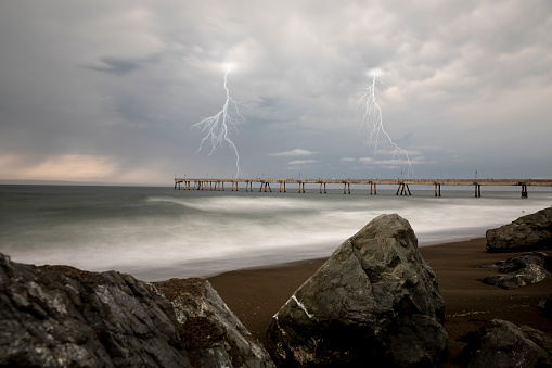 High quality stock photo of a lightning strikes off the Pacific coast near a pier.