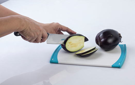 Housewife cutting eggplant with knife on a cutting board on white background