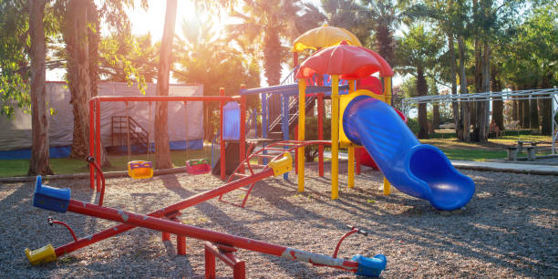 children playground with colorful swing and plastic slide on sand in public park children playground with colorful swing and plastic slide on sand in public park sunlight background swing play equipment photos stock pictures, royalty-free photos & images