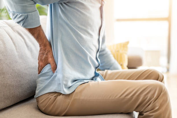 Unrecognizable mature man having backache. Close-up of unrecognizable senior man having back pain while sitting in the living room. lower back pain stock pictures, royalty-free photos & images