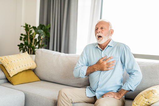Worried senior man feeling unwell and having chest pain in the living room.