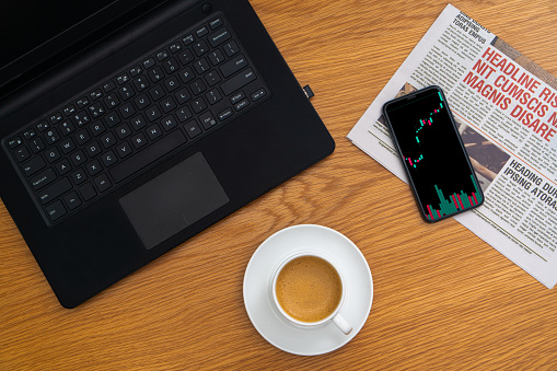 A coffee cup at work with laptop, smartphone and chart of trading, stock market, newspaper,...