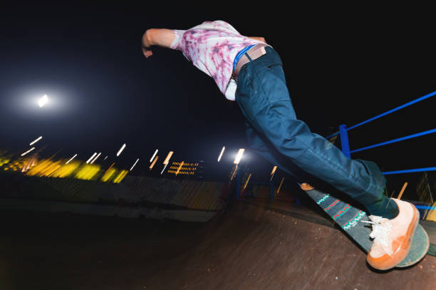 a young skater at night in a skatepark does the trick on the railing. x-ray culture nightlife concept - rolling up flash imagens e fotografias de stock