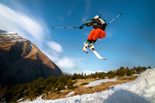 istock man skier in flight after jumping from a kicker in the spring against the backdrop of mountains and blue sky. Close-up wide angle. The concept of closing the ski season and skiing in spring 1267639616