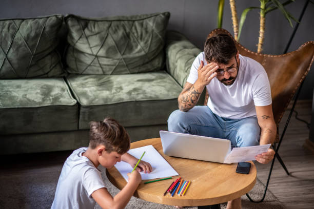 istock Father and son in the living room, father working on laptop while son spends time creatively - drawing on paper 1267639665