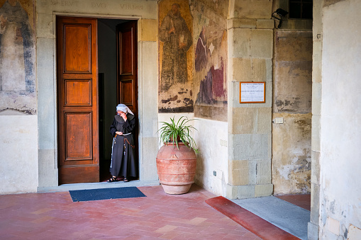 Florence, Italy, August 12 -- A nun comes out of the main door of an ancient Franciscan convent in the historic center of Florence. On the walls some ancient frescoes on the life of St. Francis. Image in High Definition format.