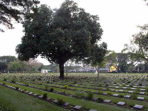 Kanchanaburi, Thailand, January 26, 2013: Graves under a tree at the World War II Army Fighters Military Cemetery in Kanchanaburi, Thailand.