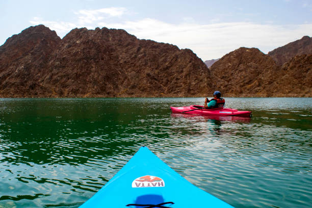 Young man is in a pink kayak in the Middle of Hatta lake and colorful blue kayak on foreground stock photo