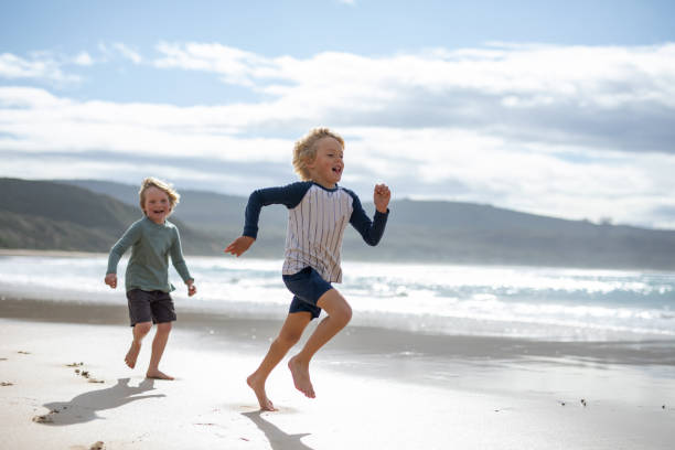 Brothers running on a beach next to the water stock photo