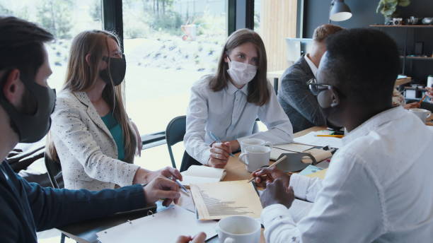 istock Workplace with epidemic safety measures. Young multiethnic business colleagues work at office table meeting, wear masks. 1267654664