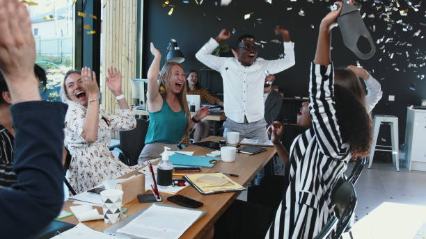 istock Coronavirus lockdown ending. Happy multiethnic business team taking masks off, celebrate victory with confetti at office 1267654744