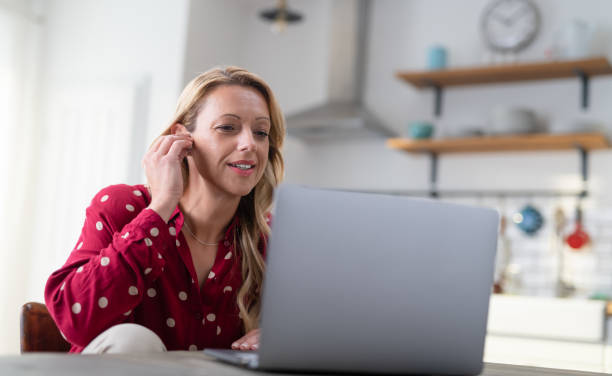 istock Beautiful Young Woman Smiling And Using Laptop While Sitting In Her Kitchen. 1267658854