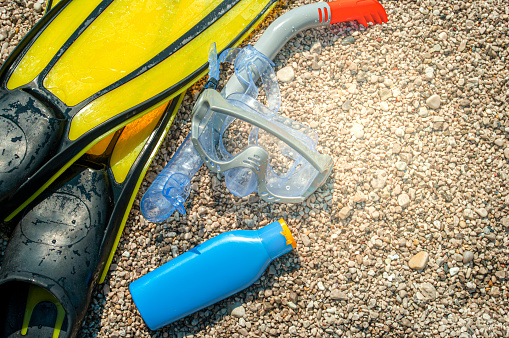 Scuba Diving Equipment and Sun Cream Bottle On The Pebble Beach