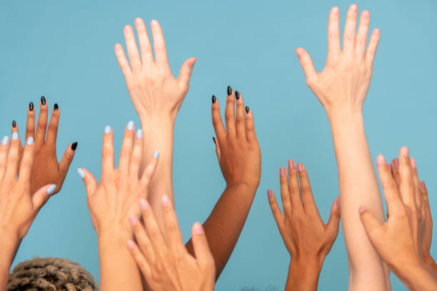 Hands of large group of women of various ethnicities with white and dark skin Hands of large group of young women of various ethnicities with white and dark skin raising arms in front of camera against blue background skin tones stock pictures, royalty-free photos & images