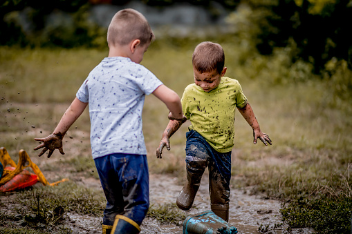 Two cute boys in rubber boots jumping in muddy puddle