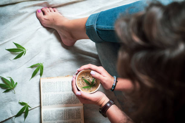 woman having marijuana infused coffee while reading a book at home top view - espresso women cup drink imagens e fotografias de stock