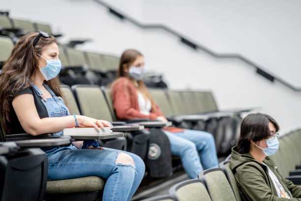 Group of university students wearing masks in class Multi-ethnic group of students wearing protective face masks while sitting in a lecture hall sitting 2 meters apart. continuing education stock pictures, royalty-free photos & images