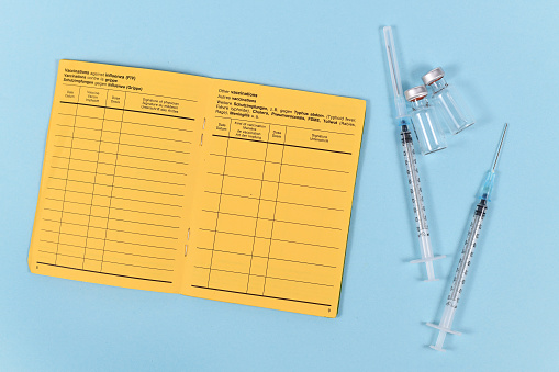 Vaccine concept with syringes, vials and empty yellow international certificate of vaccination with German and English text on blue background