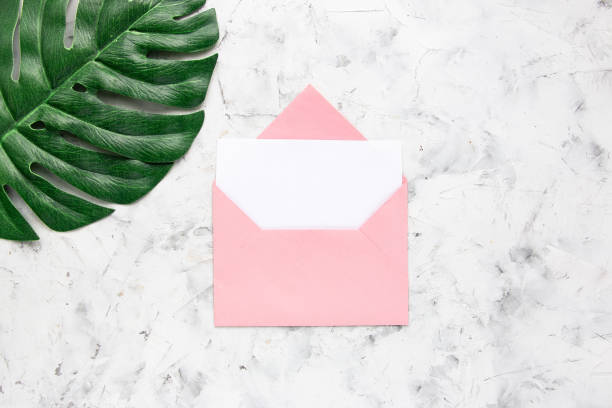 istock Pink envelope with white blank card and green monstera leaf on white concrete background. Flat lay, top view. 1267685784