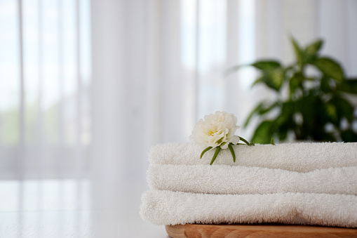 Stack of white fresh towels with white flower on wooden board. Laundry, washing or dry cleaning concept. Copy space.