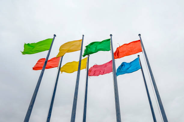 istock Plain monophonic color disheveled flags on flagpole waving on gray sky background 1267695933