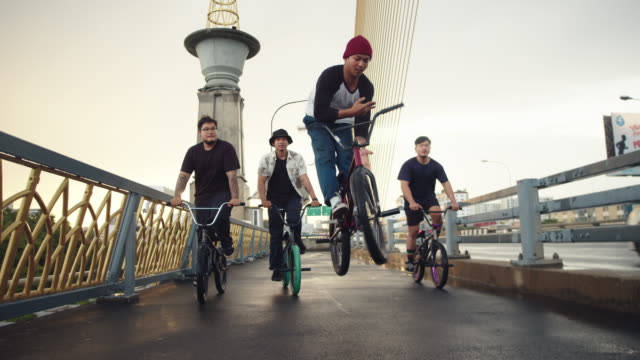 A group of BMX biker is driving through the streets of a city. They cruising around and making some tricks.