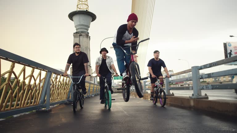 A group of BMX biker is driving through the streets of a city. They cruising around and making some tricks.