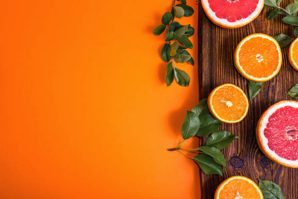 Fresh oranges and grapefruit cut in slices or halves on wooden board on orange flat lay background. Citrus fruit