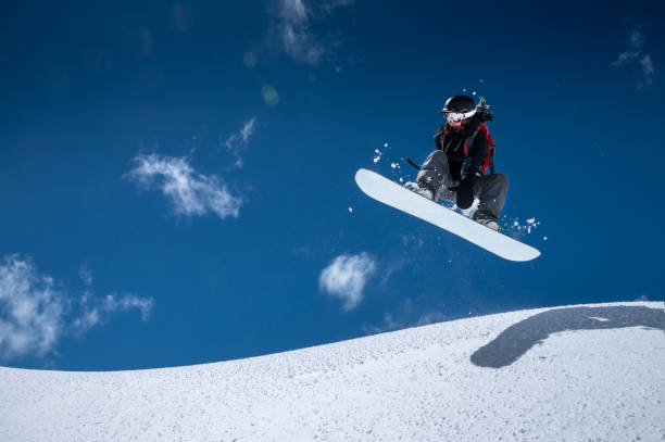 профессиональная сноубордистка в полете после прыжка со снежных карнизов делает грабли против голубого неба в солнечный день. концепция з� - ski resort winter snow blizzard стоковые фото и изображения