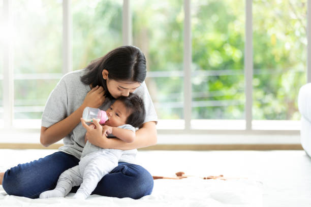 肖像画若いアジアの母親の保育園は抱き合う母親の新生児に赤ちゃんのミルクのボトルを供給します。ヘルスケアシングルママ母性ストレスの概念。 - female nurse 写真 ストックフォトと画像