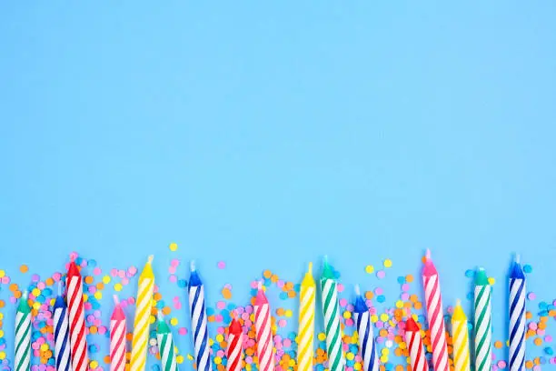 Photo of Birthday cake candles with candy sprinkles. Bottom border on a blue background.