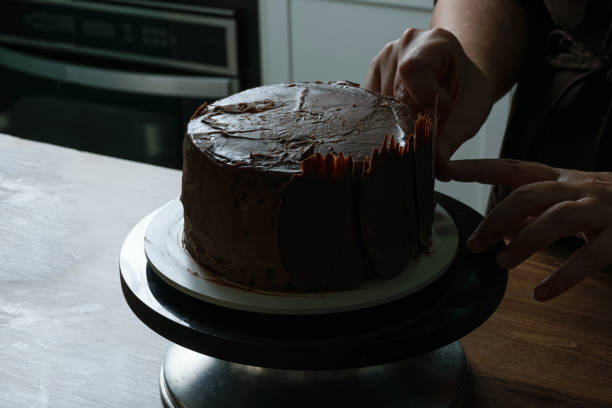 istock Chocolate cake being decorated by confectionery with chocolate plates. Main light from behind. 1267701952