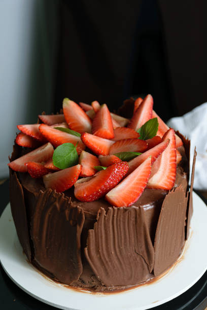 istock Chocolate cake covered with fresh strawberries, basil leaves and chocolate plates around it. 1267702216