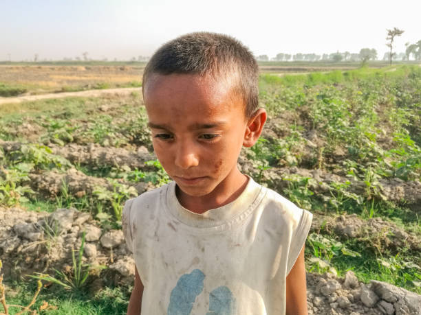 closeup of a poor staring hungry orphan boy in a refugee camp with sad expression on his face and his face and clothes are dirty and his eyes are full of pain - facial expression child asia asian and indian ethnicities imagens e fotografias de stock