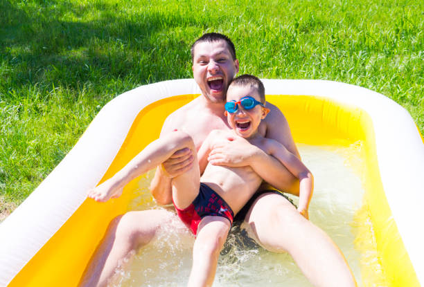 istock Dad plays with his son in the inflatable pool. Child with father are having fun, splashing, laughing in the outdoor pool. Father's day. 1267711394