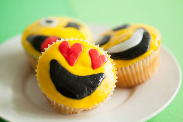 A selection of smiley face iced homemade cup cakes in a tray on a kitchen table