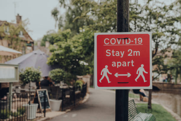 красный covid-19 оставайтесь 2 метра помимо знака на тротуаре в буртон-он-воды, котсуолдс, великобритания. - cotswold стоковые фото и изображения