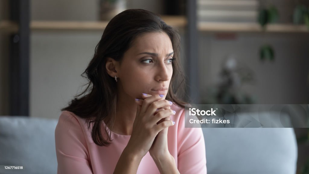 Anxious Arabic woman feel unhappy thinking at home Worried young indian Arabic woman sit on couch at home look in distance thinking pondering, anxious unhappy arab mixed race female suffer from mental psychological personal problems, mourn or yearn Women Stock Photo