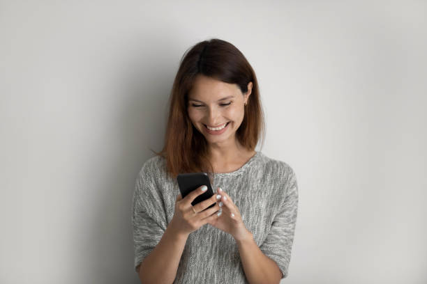 istock Smiling woman isolated on grey background using cellphone 1267719496