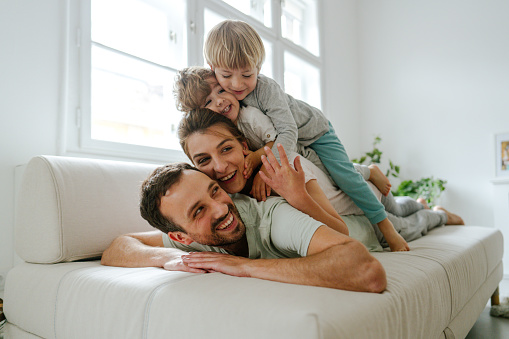 Photo of a young family with two kids lying on the top of each other being cheerful and playful; morning routine of a young modern family.