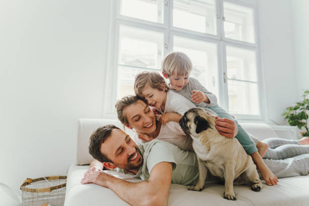 Lovely mornings Photo of a young family with two kids lying on the top of each other being cheerful and playful; accompanied by their dog who is sitting next to them; morning routine of a young modern family. young family stock pictures, royalty-free photos & images