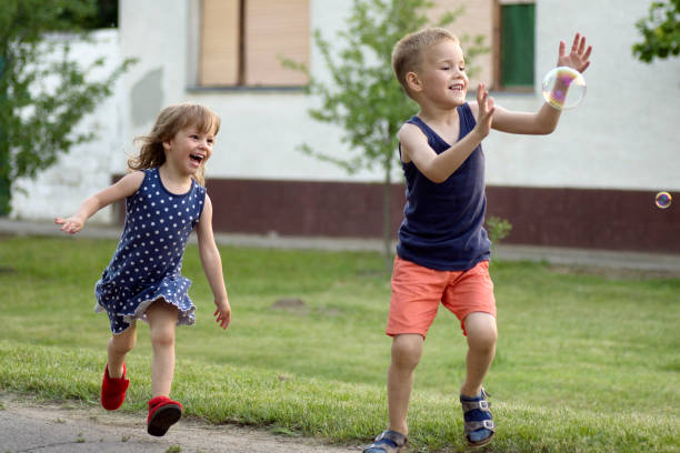 Playful running happy children, six years old boy and three years old girl are playing outdoors, carefree cheerful childhood.